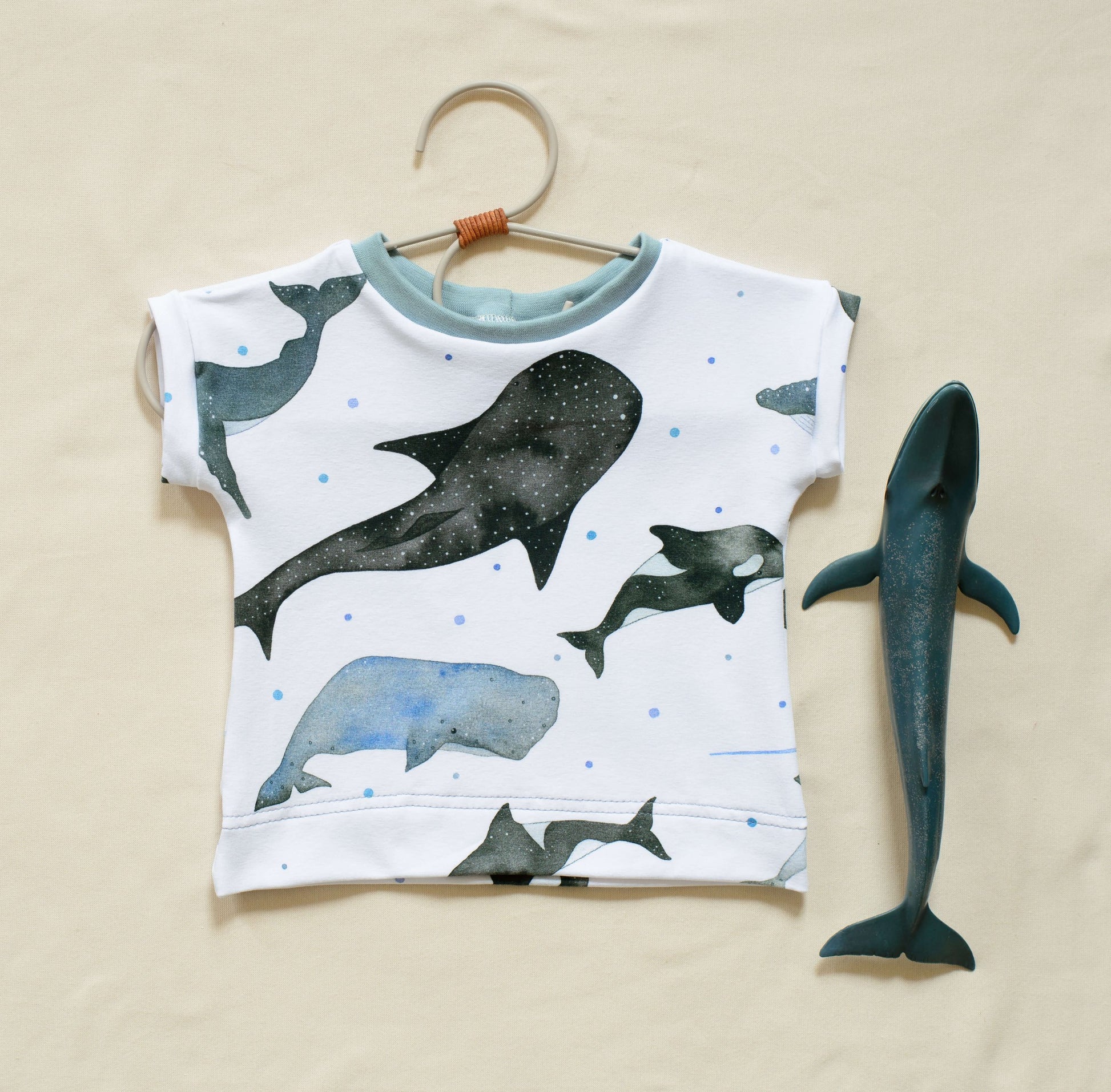 Organic whale short sleeve tee displayed on a coat hanger next to a toy whale