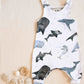 Organic whales romper with one open shoulder displayed next to shells and pebbles