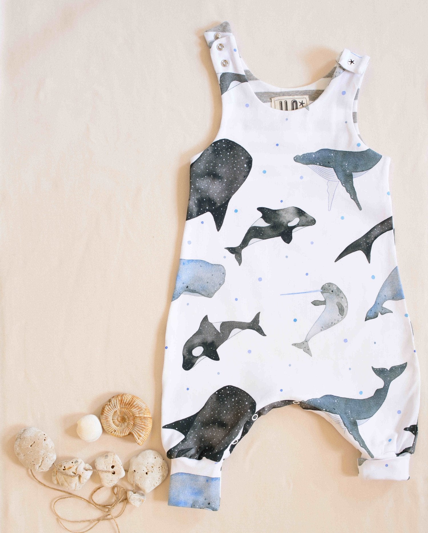 Organic whales romper with one open shoulder displayed next to shells and pebbles